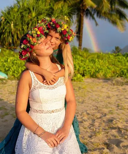 Two women standing on a beach with flowers in their hair.