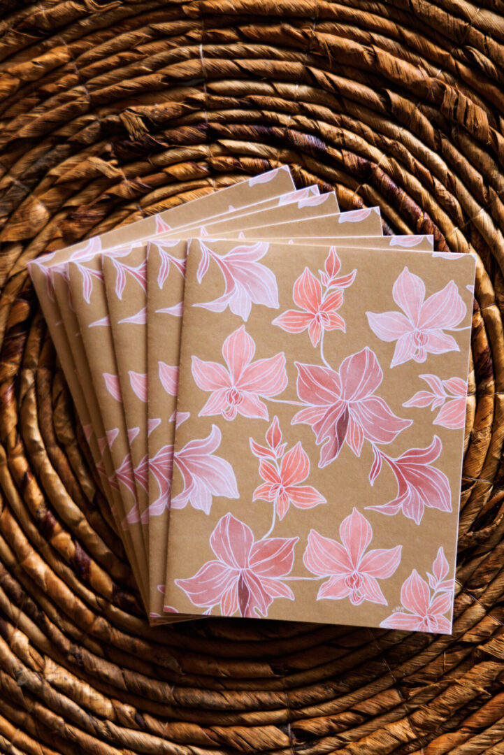 A set of five notebooks with pink leaves on them.