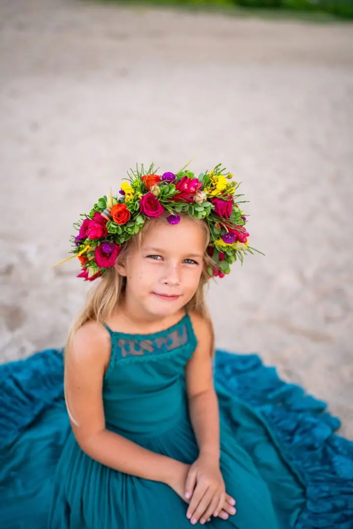 A little girl sitting on the ground wearing a flower crown.