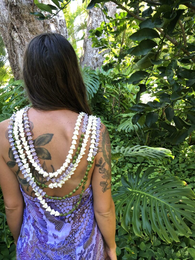 A woman with tattoos and necklaces in the woods.